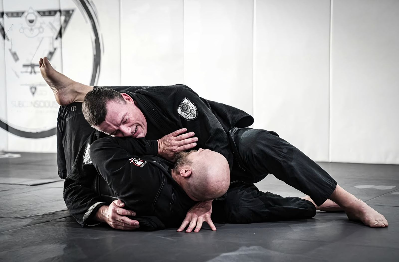 Coach Rob Grant, BJJ black belt, rolling with a training partner on the mat, both wearing black gis